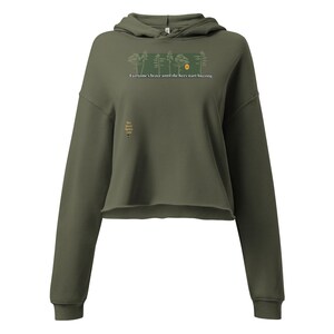 Può includere: Felpa con cappuccio corta verde oliva con cappuccio con coulisse e maniche lunghe. La parte anteriore presenta una grafica rettangolare con alberi e un sole, e il testo "Everyone's brave until the bees start buzzing." Una grafica più piccola è in basso a sinistra.