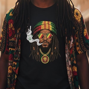 Peut inclure: T-shirt noir avec une illustration détaillée d'un homme avec des dreadlocks, portant un chapeau et des lunettes de soleil de style rastafari. Le graphisme comprend un signe de paix et un pendentif lion. La chemise est associée à une chemise boutonnée à motifs colorés.