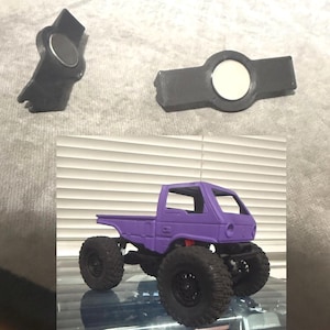 May include: A purple toy pickup truck with large black tires. Two black plastic pieces with circular white and silver accents are also shown. The truck has a detailed cab and bed design, suitable for a child's play.