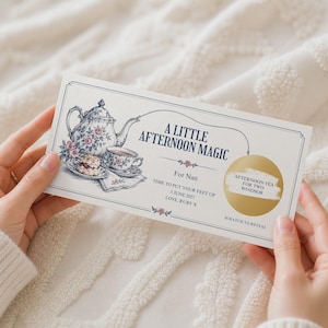 Puede incluir: Un vale de regalo rectangular titulado A LITTLE AFTERNOON MAGIC con una ilustración vintage de una tetera, una taza de té y un bollo con flores. Incluye un panel dorado para rascar, el texto For Nan, 5 JUNE 2027, LOVE, RUBY X y SCRATCH TO REVEAL.