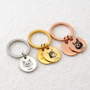May include: Three personalized cat keychains in silver, gold, and rose gold. Each keychain features a round pendant with a detailed engraved cat portrait and a name. One gold keychain has the text "N 11 years".