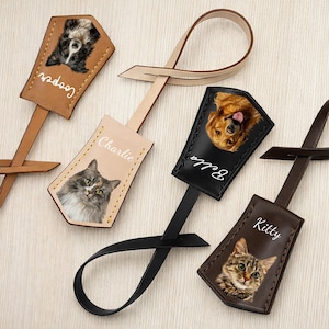 May include: Leather pet luggage tags featuring photos of dogs and cats. Each tag has a different pet's name in white script. The tags are in various colors, including brown, black, and tan, with a loop for attaching to luggage.