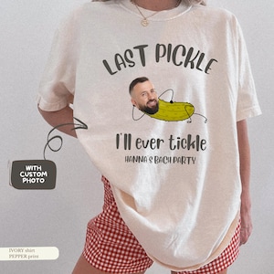 Peut inclure: T-shirt de couleur ivoire avec l'inscription "LAST PICKLE" au-dessus d'un dessin de cornichon avec un visage d'homme. Le texte "I'll ever tickle HANNA'S BACH PARTY" est en dessous. Option photo personnalisée.