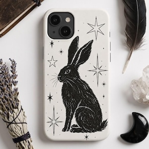 May include: A white smartphone case featuring a black ink-style illustration of a rabbit sitting in profile. The design includes various four-pointed and eight-pointed stars surrounding the rabbit, creating a celestial aesthetic on the back cover.
