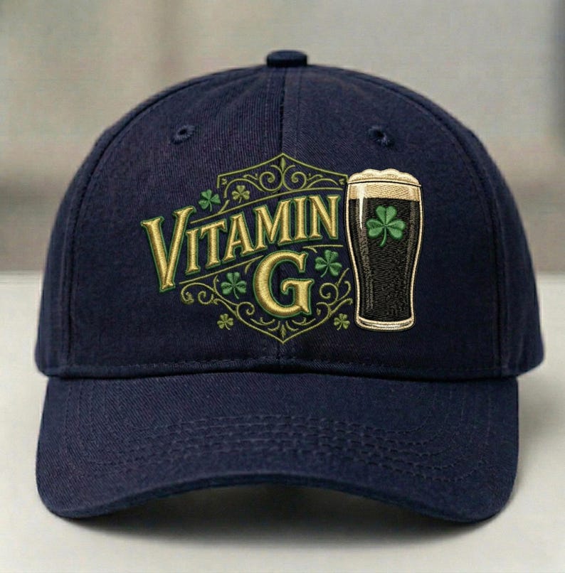 May include: Navy blue baseball cap featuring the text "Vitamin G" in gold lettering, along with a graphic of a pint of dark beer with a shamrock. The cap has a curved brim and a button on top.