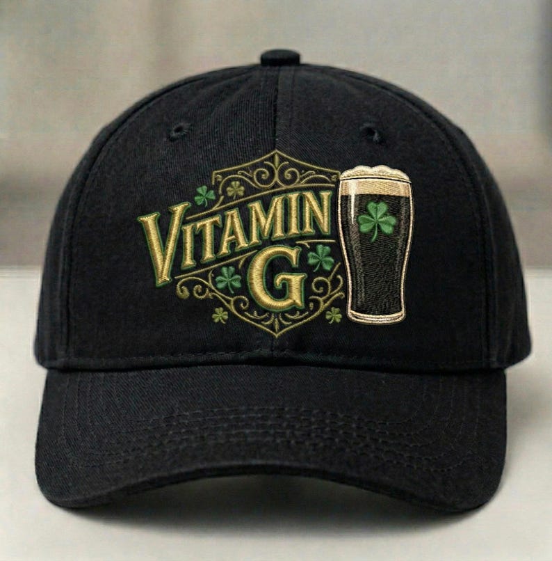 May include: Black baseball cap with the text "Vitamin G" in gold lettering, featuring shamrocks and a pint of dark beer with a shamrock. The cap has a curved brim and a button on top.