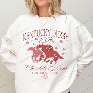 May include: White sweatshirt with a maroon graphic featuring the text "Kentucky Derby 152th" and "Churchill Downs". The graphic includes images of horses racing and roses. The sweatshirt is a casual style.