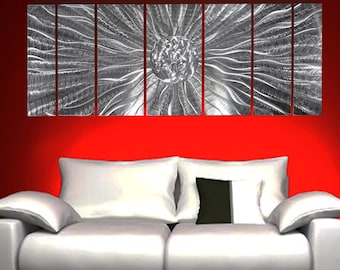 May include: A seven-panel silver metal wall art piece featuring a central circular motif with radiating textured lines. The metallic surface displays a brushed finish that catches light, creating a dynamic pattern across the individual rectangular panels.