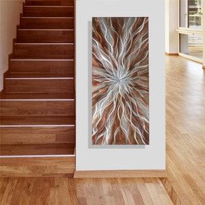 May include: Abstract metal wall art with a swirling, organic design in shades of copper and silver. The piece has a textured, three-dimensional look.