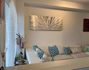 May include: A white sectional sofa with blue and white patterned pillows in a modern living room with a large metal wall art piece above the sofa.
