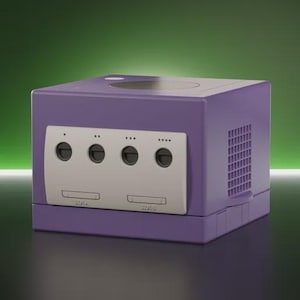 Pode incluir: Uma consola de videojogos roxa em forma de cubo com um painel frontal cinzento-claro, quatro portas para comandos, duas ranhuras para cartões de memória e uma tampa circular para o disco na parte superior, com grelhas de ventilação laterais.