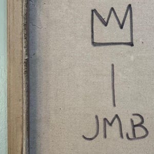 May include: A close-up of a canvas with a black crown drawing above a vertical line. Below the line are the black letters "JMB". The canvas has a beige color and is framed with a brown border.