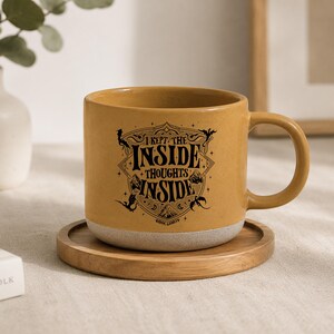 May include: A mustard yellow ceramic mug with a speckled texture and a light gray base. The front features a black graphic design with the text I KEPT THE INSIDE THOUGHTS INSIDE, surrounded by decorative line art of dragons and mountains.