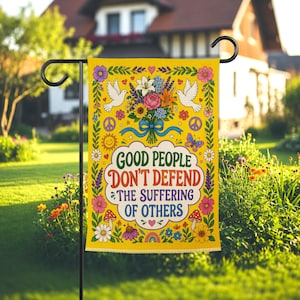 May include: A yellow garden flag with a floral design and the text "GOOD PEOPLE DON'T DEFEND THE SUFFERING OF OTHERS." The flag features a bouquet of flowers, doves, mushrooms, and a peace symbol.