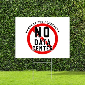 May include: A white yard sign with the text "PROTECT OUR COMMUNITY" in a circular arc, surrounding a red circle with a line through it. Inside the circle are the words "NO DATA CENTER" in black. The sign is on a metal frame, placed on green grass.