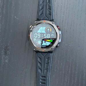 May include: Black smartwatch with a digital display showing the time as 09:58. The watch has a black strap with a textured design. The watch face displays various data points, including the date and battery life.