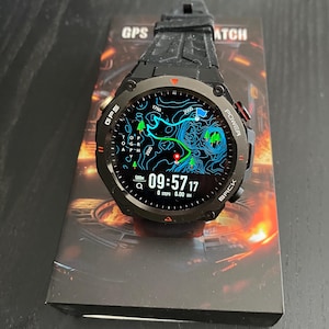 May include: Black GPS watch with a digital display showing a map and time. The watch has a black strap and is on top of a box with the words "GPS WATCH". The display shows the time as 09:57:17.