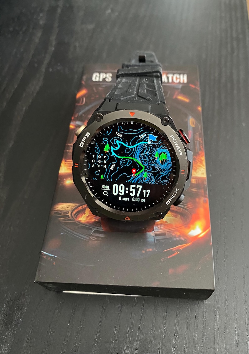 May include: Black GPS watch with a digital display showing a map and time. The watch has a black strap and is on top of a box with the words "GPS WATCH". The display shows the time as 09:57:17.