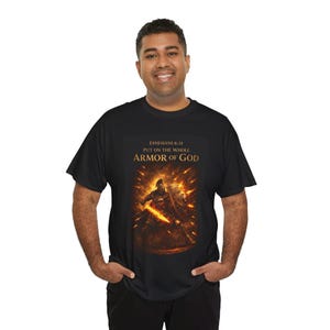 Peut inclure: T-shirt noir avec un motif de guerrier, une épée et un bouclier sur fond de feu. Le texte "Éphésiens 6:11 Revêtez toute l'armure de Dieu" est imprimé. Le t-shirt est porté par une personne.