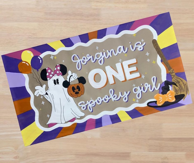 Op de afbeelding: Een rechthoekig, handgeschilderd bord met een Halloween-thema. Het bord toont een geest verkleed als Minnie Mouse met een pompoen en ballonnen. De tekst luidt "Jorgina is ONE spooky girl" in witte letters. Een heksenhoed en een bezem zijn ook afgebeeld.