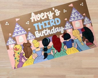 May include: A rectangular sign featuring the text Avery's THIRD Birthday in white and blue lettering. The background displays a brown castle with purple roofs and eight illustrated figures with various hair colors and dresses standing in a row.