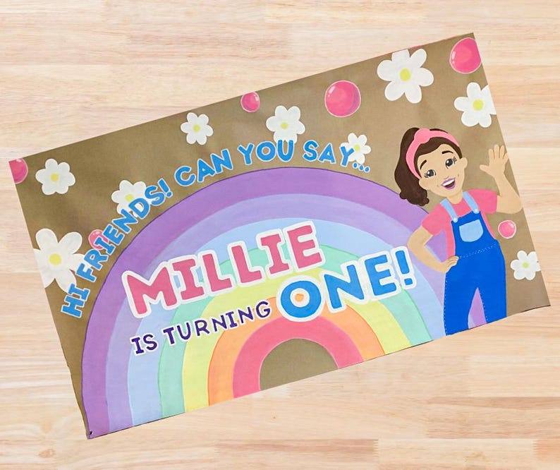 Op de afbeelding: Een bruine papieren uitnodiging met een regenboog, madeliefjes en de tekst "Millie is turning ONE!". Een cartoonmeisje in een blauwe overall zwaait. De tekst "Hi friends! Can you say..." is ook aanwezig.