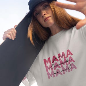 May include: White t-shirt with the word "MAMA" in pink, stacked three times with the names "Alexandra" and "Samuel" below. A black skateboard is held over the shoulder.
