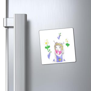 Könnte beinhalten: Ein quadratischer Magnet mit einer Kinderzeichnung einer Person mit rosa Schal, blauem Kleid und goldenem Stirnband. Die Zeichnung ist von Blumen und lila Akzenten umgeben. Der Magnet befindet sich auf einem silbernen Kühlschrank.