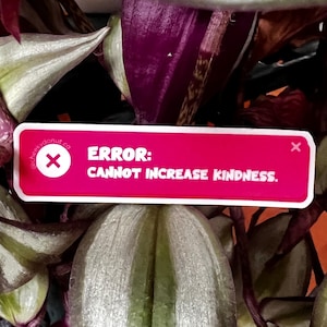 May include: A pink rectangular sticker with white text that reads "ERROR: CANNOT INCREASE KINDNESS." A white "X" is in the upper corners. The sticker is set against a backdrop of green and purple plant leaves, creating a contrasting visual.