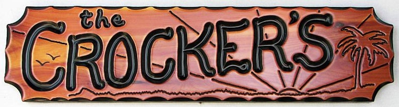 May include: A wooden sign with a sunset scene and a palm tree. The sign reads "the CROCKER'S" in black lettering.