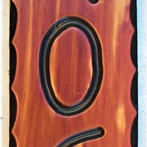 May include: A wooden house number sign with black numbers. The numbers are 34063. The sign is a reddish brown color and has a scalloped edge.