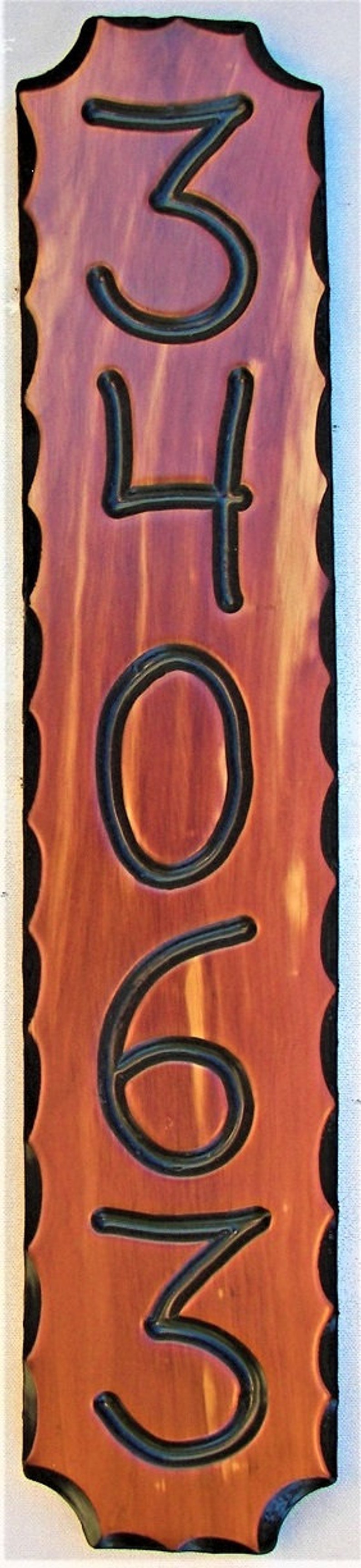 May include: A wooden house number sign with black numbers. The numbers are 34063. The sign is a reddish brown color and has a scalloped edge.