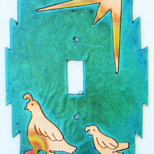 Könnte beinhalten: Ein türkisblauer Lichtschalter aus Keramik mit einem stilisierten Kupferblitz-Design und zwei Wachtel-Silhouetten.