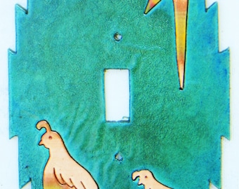 Può includere: Una placca per interruttore della luce in ceramica blu turchese con un design a fulmine in rame stilizzato e due silhouette di quaglie.