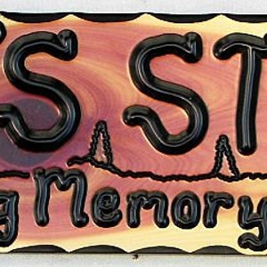 May include: A wooden sign with the text "Dad's Stand In Loving Memory of Jerry" in black lettering. The sign has a rustic, natural wood grain and a brown background with a red-brown swirl in the center.