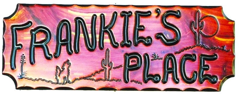May include: A wooden sign with a pink and orange background. The sign says "Frankie's Place" in black letters with a blue outline. The sign has a rustic, southwestern design with cacti and a sun.