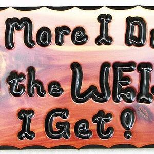 May include: A wooden sign with a red-brown stain and black lettering that reads "The More I Drink Bud the Weiser I Get?" The sign has a decorative border and two bottle silhouettes.