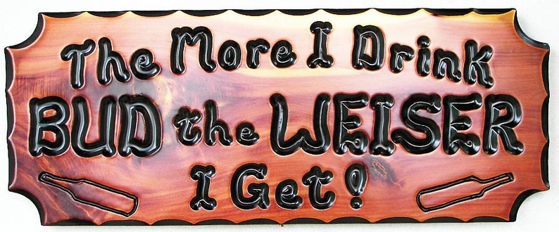May include: A wooden sign with a red-brown stain and black lettering that reads "The More I Drink Bud the Weiser I Get?" The sign has a decorative border and two bottle silhouettes.