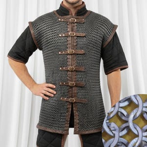 Puede incluir: Un chaleco de cota de malla de estilo medieval con detalles y correas de cuero marrón. El chaleco se usa sobre una camisa negra de manga corta y pantalones cortos acolchados. La cota de malla está hecha de pequeños anillos metálicos entrelazados.