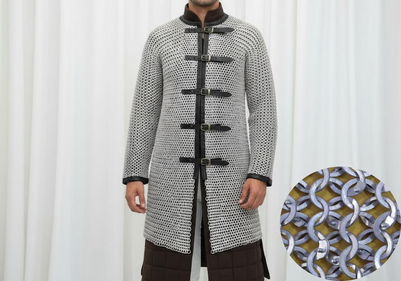 May include: A silver chainmail coat with black leather accents and buckles. The long-sleeved coat features a high collar and is worn over brown quilted pants. A close-up shows the chainmail construction.