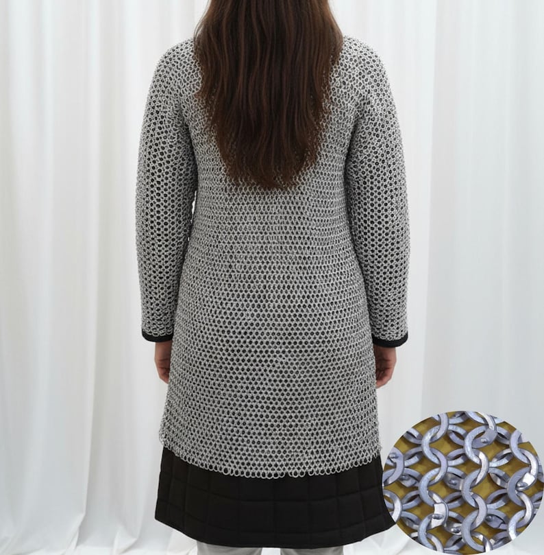 May include: A silver chainmail coat with long sleeves and a knee-length hem. The coat has a black trim at the cuffs and hem. The lower portion of the coat is black and quilted. The image shows the back of the coat.