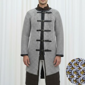May include: A silver chainmail coat with black leather accents and buckles. The long-sleeved coat has a high collar and is worn over a brown and white outfit. A close-up shows the intricate metal ring construction.