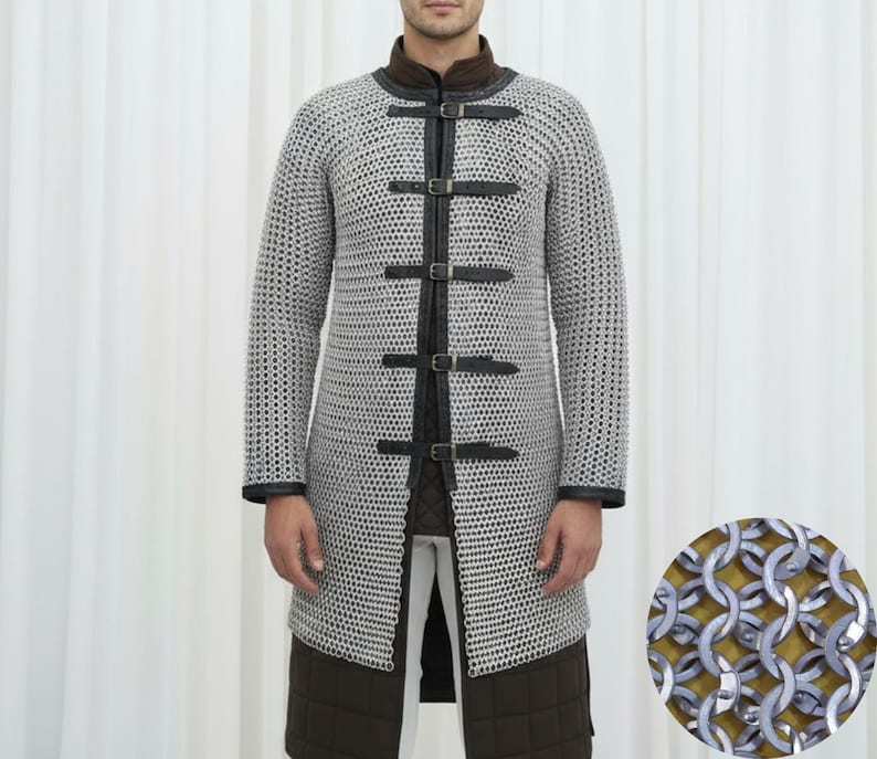 May include: A silver chainmail coat with black leather accents and buckles. The long-sleeved coat has a high collar and is worn over a brown and white outfit. A close-up shows the intricate metal ring construction.
