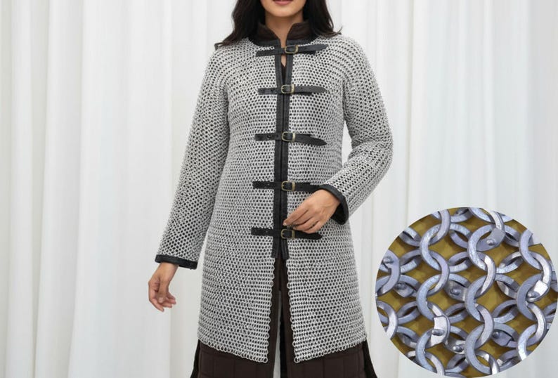 May include: A silver chainmail coat with black leather accents and buckles. The long-sleeved coat has a high collar and is fastened with leather straps. A close-up shows the interlocking metal rings.