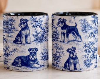 May include: Two ceramic mugs with a black handle and interior, featuring a blue and white toile pattern. The design displays illustrations of Schnauzer dogs in various poses, including sitting and lying down, surrounded by trees and foliage.
