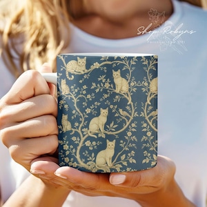 May include: White ceramic mug featuring a navy blue background with a repeating pattern of beige cats perched on flowering branches. The mug has a white handle and the text "Shop Robyn's Personal Gift" is visible.