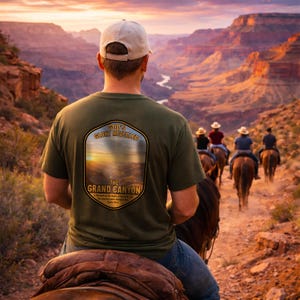 Könnte beinhalten: Olivgrünes T-Shirt mit einer Grafik des Grand Canyon und dem Text "God's Glory Revealed" und "The Grand Canyon". Das Bild zeigt eine Person auf einem Pferd, mit anderen Reitern auf einem Weg im Hintergrund.