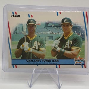 May include: A Fleer baseball card featuring Mark McGwire and Jose Canseco of the Oakland Athletics. The card is titled Oakland's Power Team and shows both players in green and yellow uniforms holding bats on a baseball field inside a plastic case.