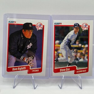 May include: Two 1990 Fleer baseball cards in protective plastic cases. The left card features Dave Righetti, a New York Yankees pitcher, and the right card features Steve Sax, a New York Yankees second base player. Both cards have red borders.