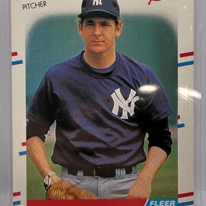 May include: A Fleer baseball card featuring Dave Righetti, a pitcher for the New York Yankees. The card displays the player wearing a dark blue jersey with a white NY logo, a matching cap, and a baseball glove, with the text Dave Righetti PITCHER.